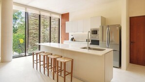 Una cuina moderna amb una illa central, tamborets de bar, electrodomèstics d'acer inoxidable i grans finestres.
