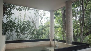 Une pièce dotée d’une piscine à fond de verre, de grandes colonnes et offrant une vue sur une végétation luxuriante.