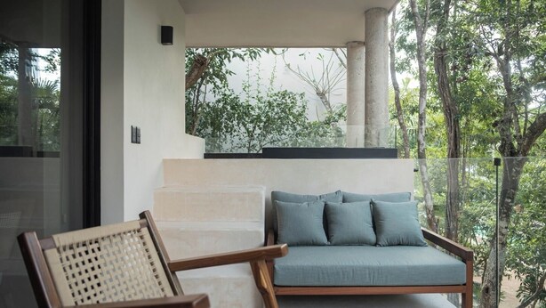 Un espace extérieur moderne aménagé avec un canapé et des fauteuils, un escalier et une vue sur la verdure.