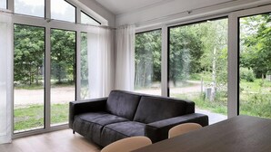 Un soggiorno moderno con un divano grigio scuro, un tavolo da pranzo in legno e ampie finestre che si affacciano su un paesaggio verde.