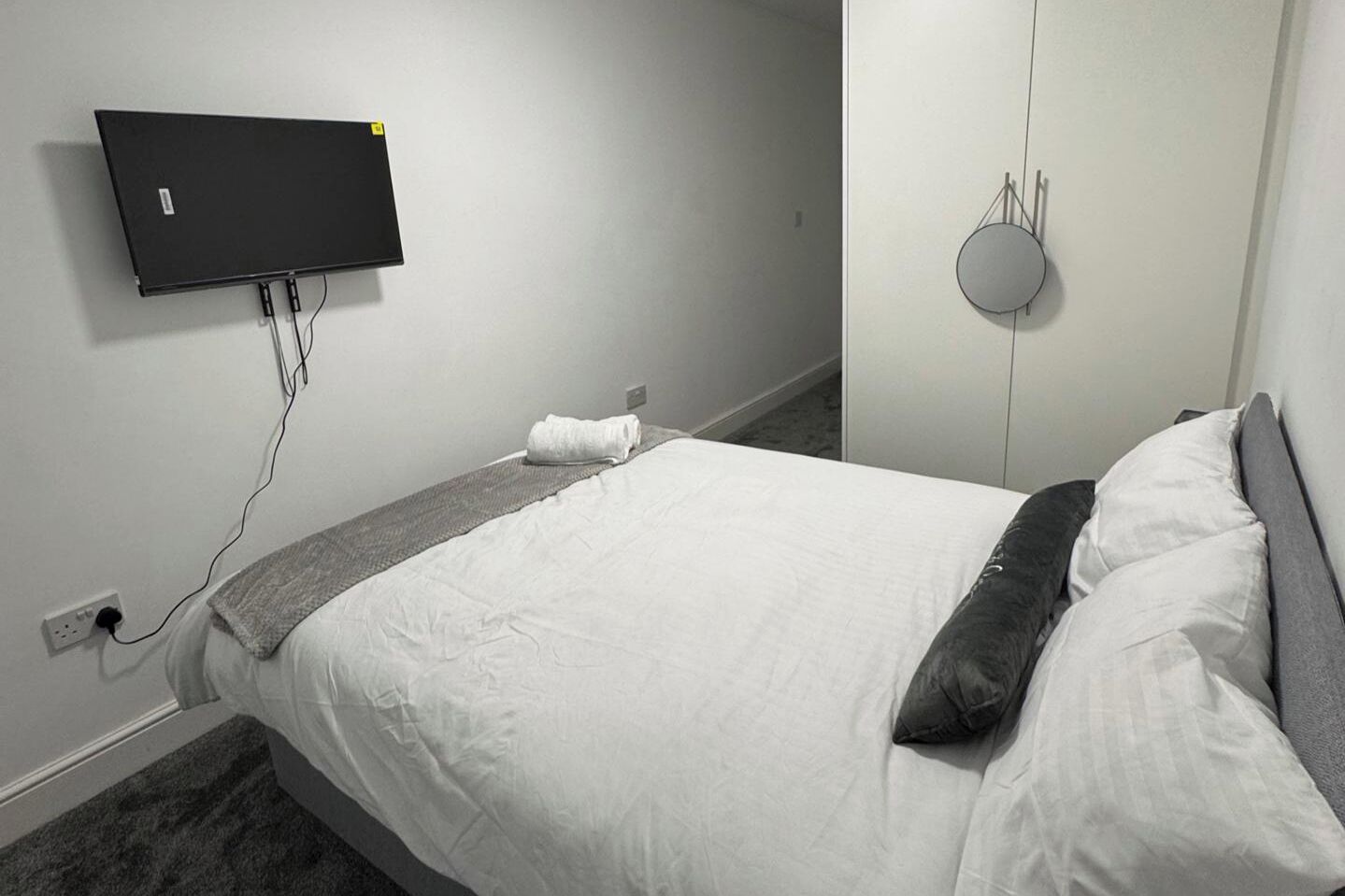 Habitación de hotel con cama, televisor de pantalla plana montado en la pared, toma de corriente e iluminación empotrada.
