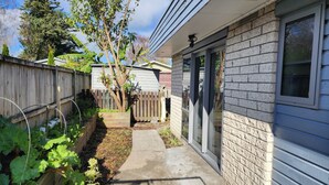 A residential backyard with a wooden fence, a concrete pathway, and a brick house with a window.