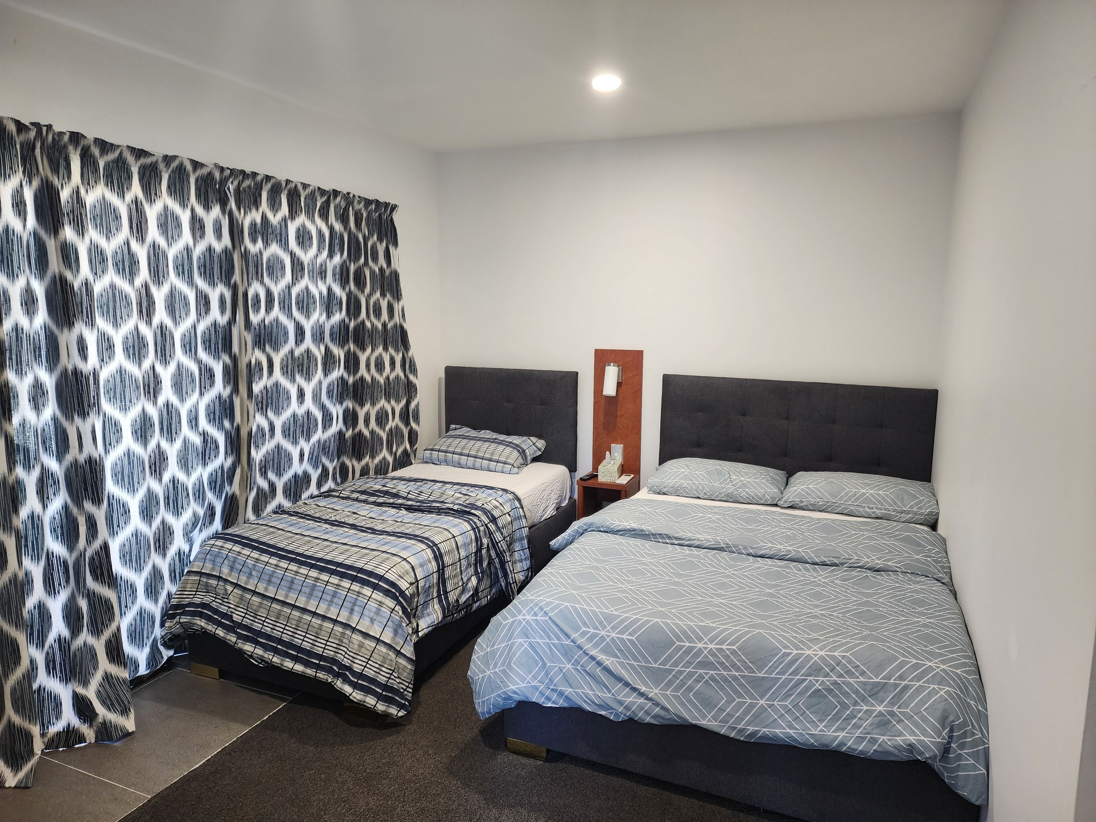 Een hotelkamer met twee bedden, een nachtkastje, een aan de muur bevestigd telefoon en een gordijn met een geometrisch patroon.