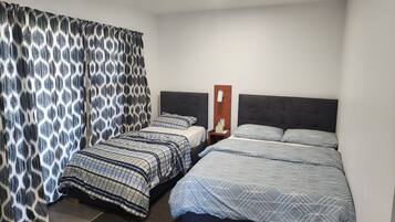 Een hotelkamer met twee bedden, een nachtkastje, een aan de muur bevestigd telefoon en een gordijn met een geometrisch patroon.