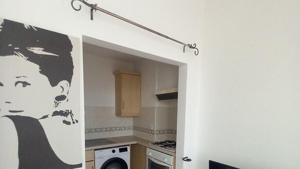 A compact kitchen with a washing machine, oven, and a TV on a stand. - Apartment Sleeps 2 with Parking & Garden (Greater London)
