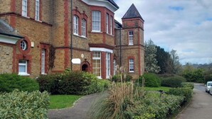 A large brick building with a tower, multiple windows, and a pathway leading to the entrance. - Apartment Sleeps 2 with Parking & Garden (Greater London)
