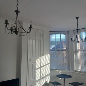 Ein Zimmer mit einer weißen Tür, einem kleinen runden Tisch und zwei Stühlen. Zwei Kronleuchter hängen von der Decke.