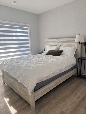 Une chambre à coucher avec un lit en bois, une table de chevet, une lampe et une fenêtre avec des stores.