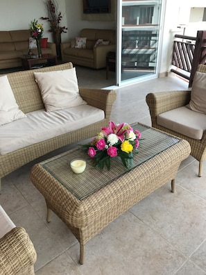 A living room with wicker furniture, a glass coffee table with flowers, and a balcony with a railing. - Two Bedroom Ocean View (Bajos de Chila)
