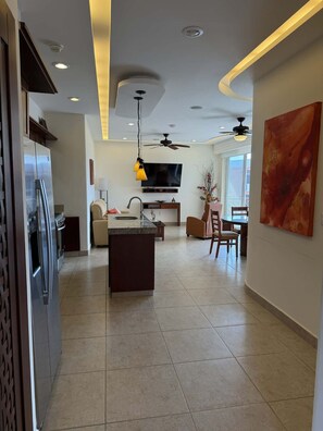 A modern kitchen with a central island, built-in appliances, and a dining area with a TV. - Two Bedroom Ocean View (Bajos de Chila)
