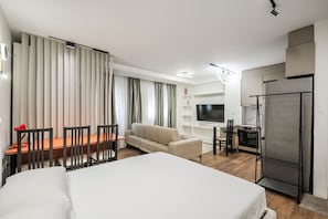 A hotel room with a bed, a dining table with chairs, a sofa, a TV, a kitchen area with a refrigerator, and a window with curtains. - City Vibes Studio Tirana Center (Tirana)
