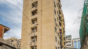 Un edificio alto e color beige con diversi balconi, una strada stretta e auto parcheggiate.