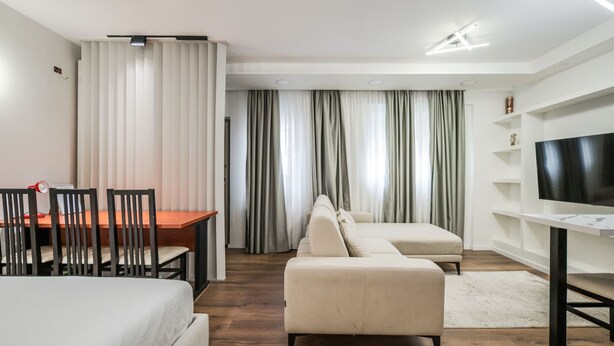 Una moderna camera d'albergo con un letto, un divano, una TV, una scrivania con sedie e un tavolo da pranzo.