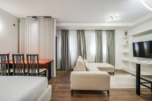 A modern hotel room with a bed, a sofa, a TV, a desk with chairs, and a dining table. - City Vibes Studio Tirana Center (Tirana)