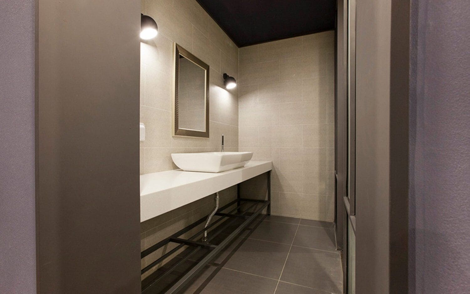 Un baño moderno con un lavamanos blanco, un espejo y dos luces fijadas a la pared.