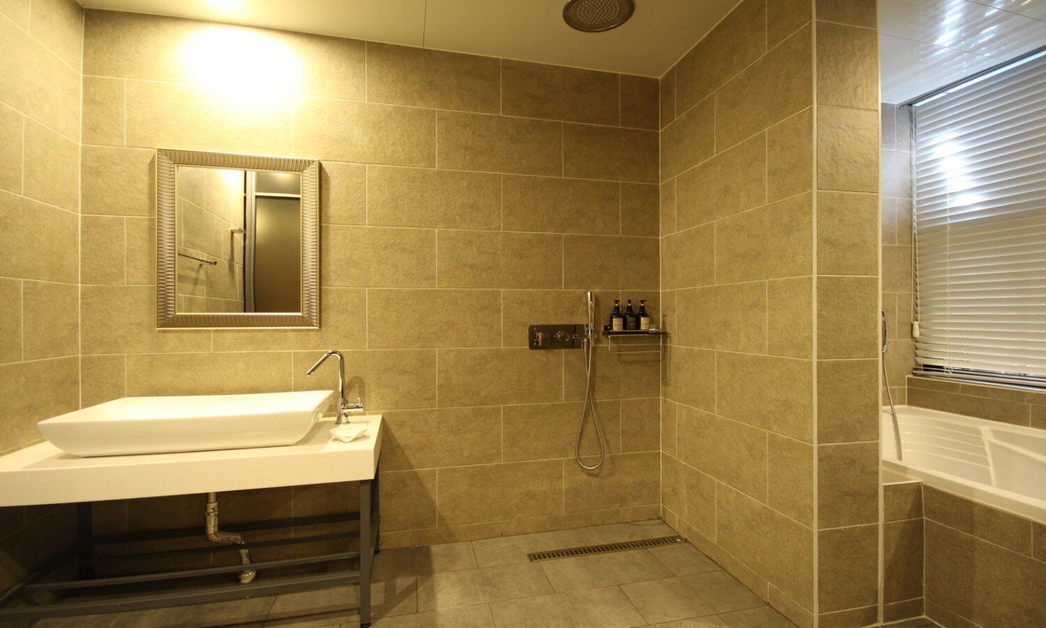 Une salle de bain équipée d’un lavabo, d’un miroir, d’une douche et d’une fenêtre avec des stores.