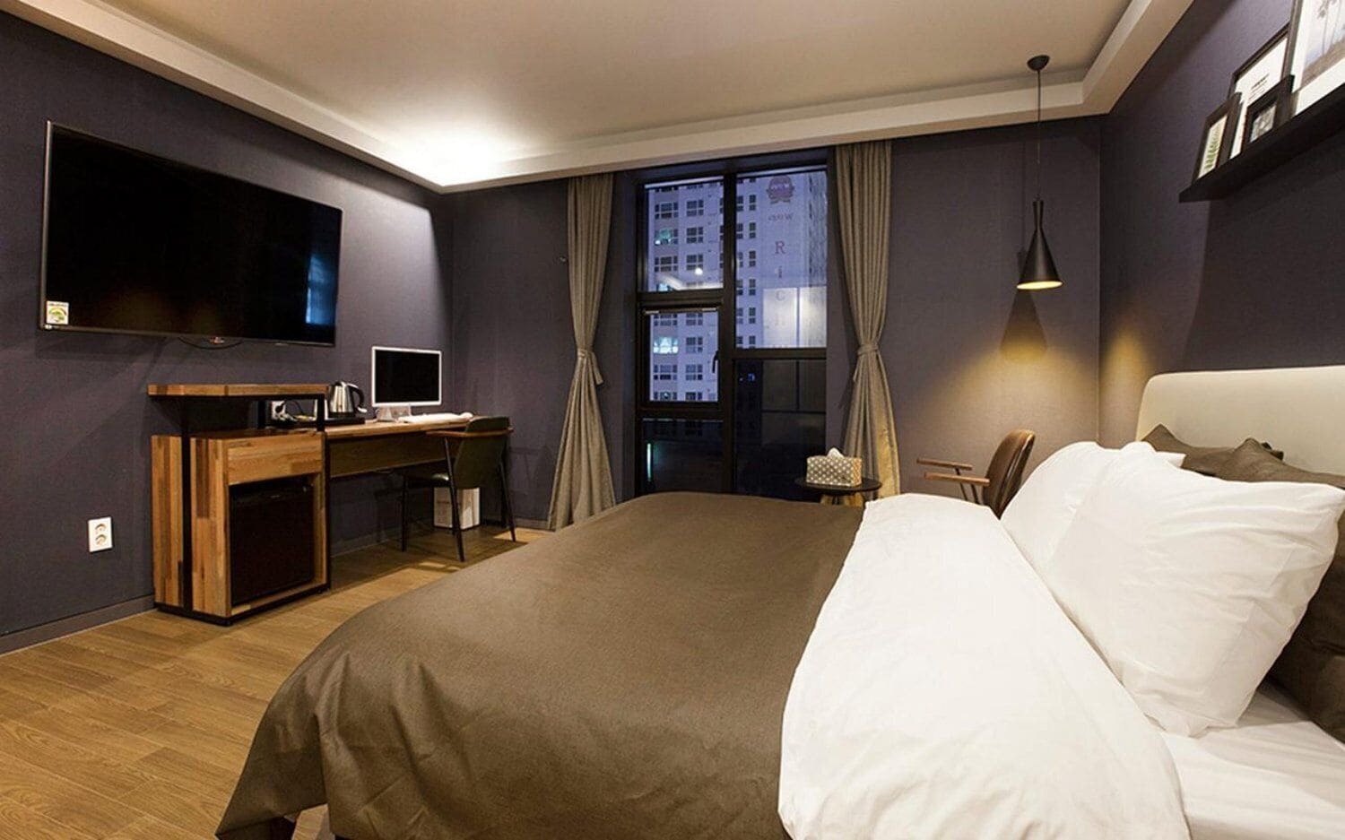 Una camera d'albergo con un letto, una scrivania, la televisione e una finestra con tende.