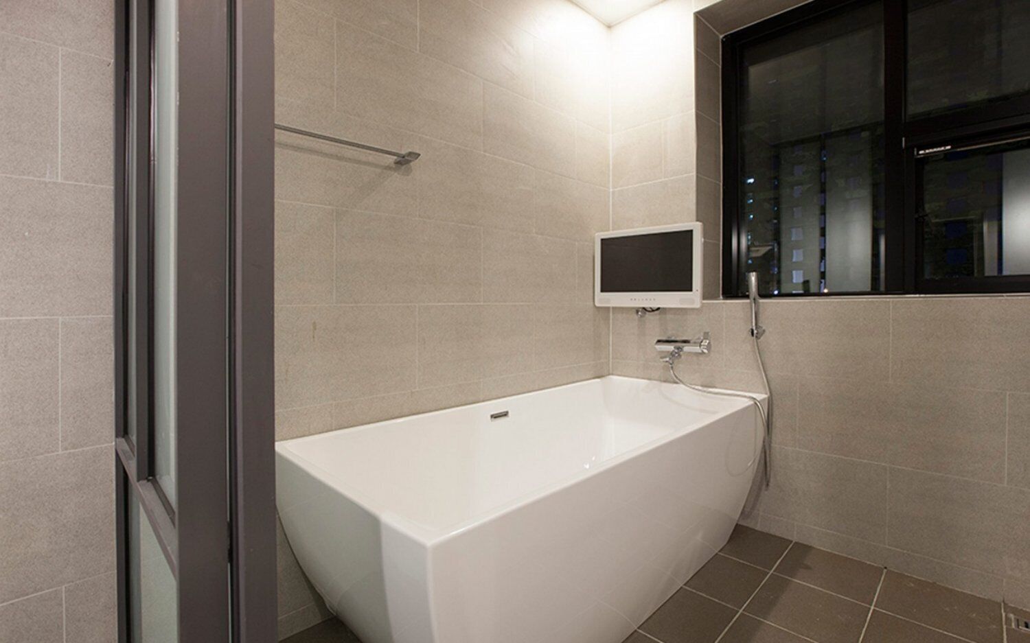 A modern bathroom with a white bathtub, a handheld showerhead, and a wall-mounted TV.