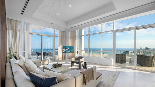 A spacious living area with a large window overlooking the sea, a comfortable sofa, a coffee table, and a TV screen. - Tresor 2-3702 (Miami Beach)