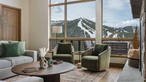Un soggiorno moderno con un'ampia finestra che si affaccia su una vista montana, un divano, due poltrone, un tavolino da caffè e una lampada.