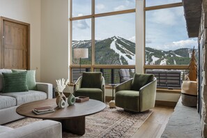 A modern living room with a large window offering a mountain view, a sofa, two armchairs, a coffee table, and a lamp. - Lakota SkiRenity | Outdoor Fire Pit | Private Hot Tub w/ Resort Views (Winter Park)