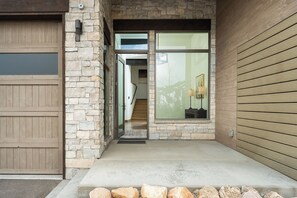 A stone exterior with a garage door, a wooden door, and a concrete entryway. - Lakota SkiRenity | Outdoor Fire Pit | Private Hot Tub w/ Resort Views (Winter Park)