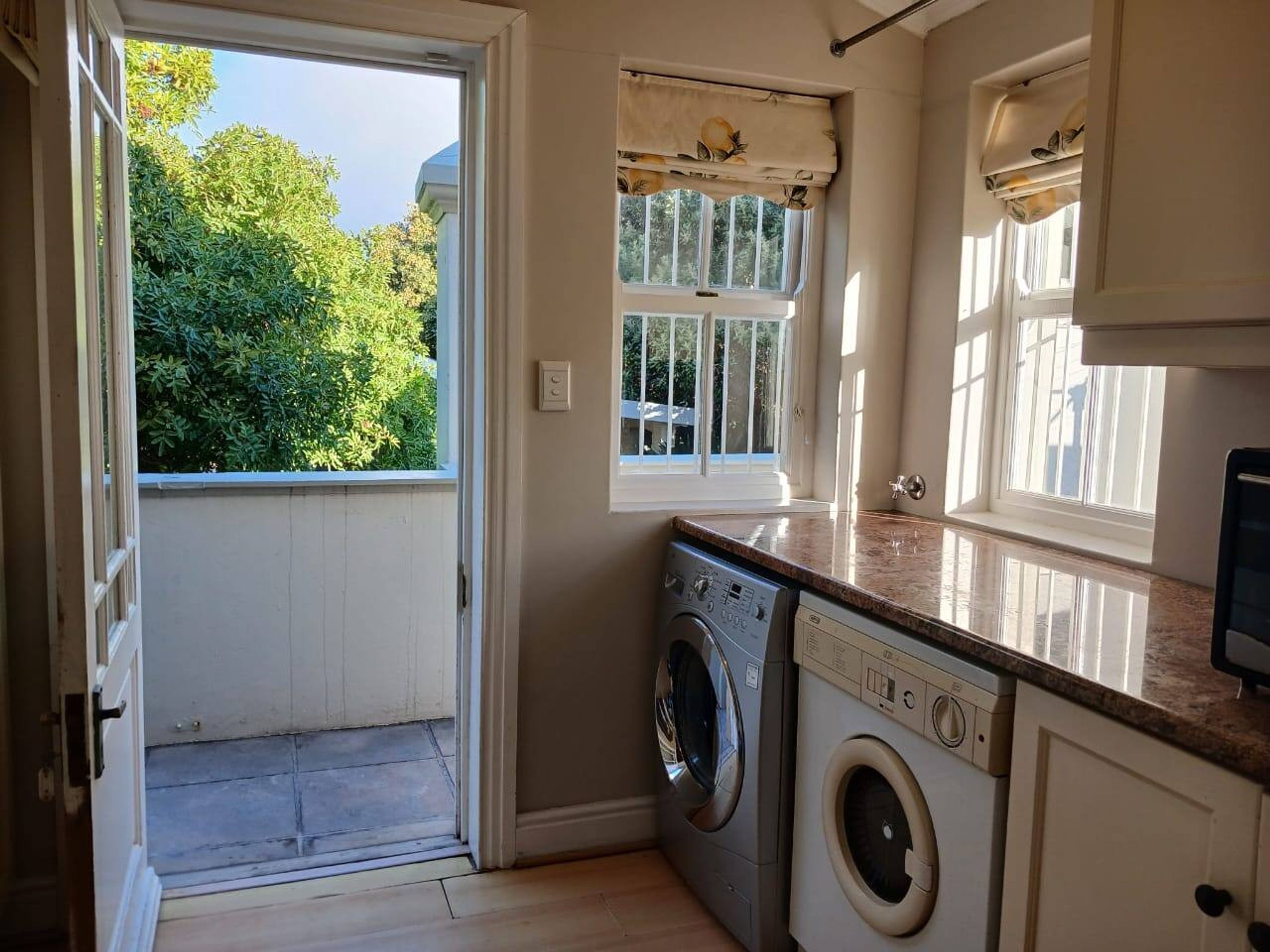 A laundry room with a washing machine and dryer, a window with curtains, and a door leading outside.