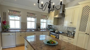 Una cocina con encimeras de granito, armarios blancos, una campana extractora de acero inoxidable y un frutero en la isla.