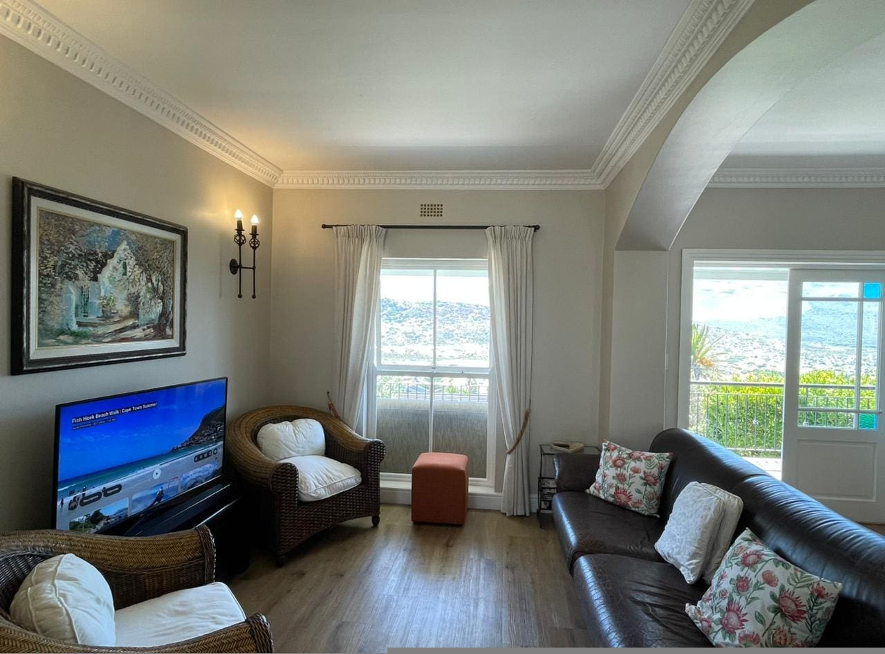 A living room with a television, wicker chairs, a sofa, and a large window with a view.