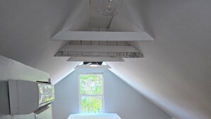 Ein Zimmer mit schrägen Wänden, einem Bett, einem Fenster und einer Lampe.