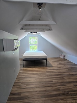 Ein Zimmer mit schrägen Wänden, einem Bett, einem Fenster und einer Lampe.