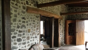 A stone-walled room with a wooden ceiling, a patterned sofa, and a red and blue patterned rug.