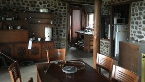 Une pièce aux murs de pierre, avec une table à manger en bois, des chaises, un coin cuisine équipé d’un réfrigérateur et d’un four à micro-ondes.