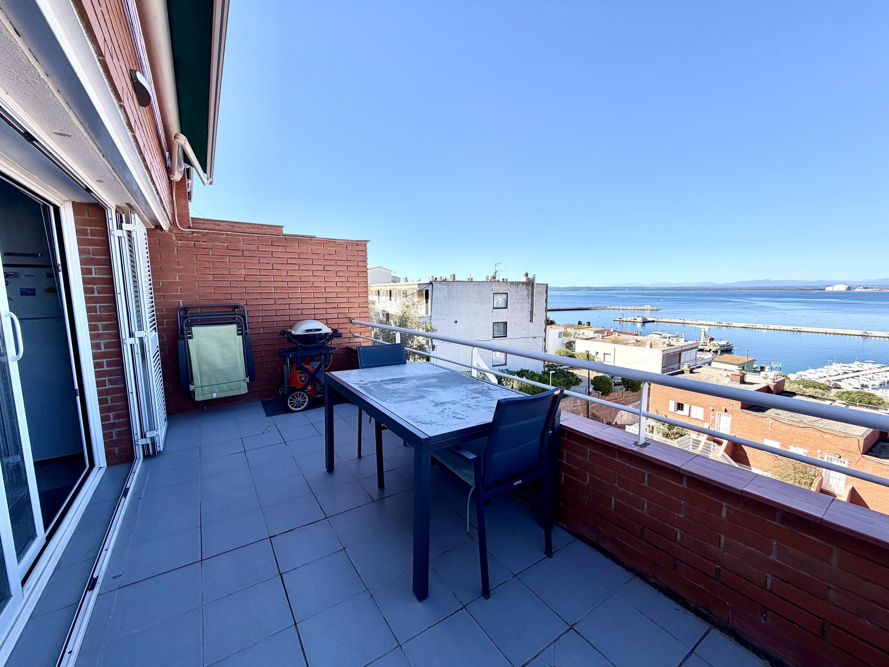 Un balcon avec une table et des chaises, un barbecue et une vue sur la mer et les bâtiments.