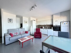 Un salon moderne avec un canapé gris, un fauteuil rouge et une table basse dont le plateau est en verre.