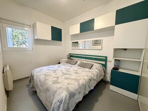 Une chambre à coucher comprenant un lit, une fenêtre, des rangements intégrés et un miroir.