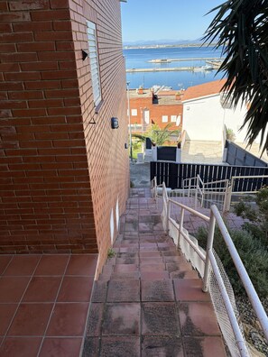 Un bâtiment en briques avec un escalier menant à une terrasse d’où l’on peut admirer un port de plaisance et des montagnes lointaines.