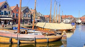 A waterfront area with traditional wooden boats docked along the canal, surrounded by historic buildings with red-tiled roofs.