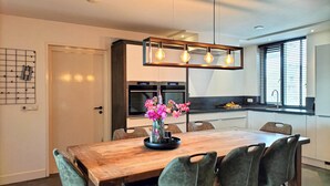 A modern kitchen with a wooden dining table, chairs, and a pendant light.
