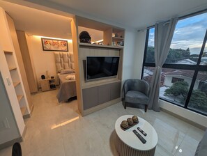 A modern living room with a flat-screen TV, a sofa, a coffee table with decorative balls, and a view of the city through large windows.