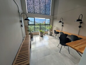 Een moderne kantoorruimte met een groot raam, zwarte stoelen, een houten bureau en potplanten.