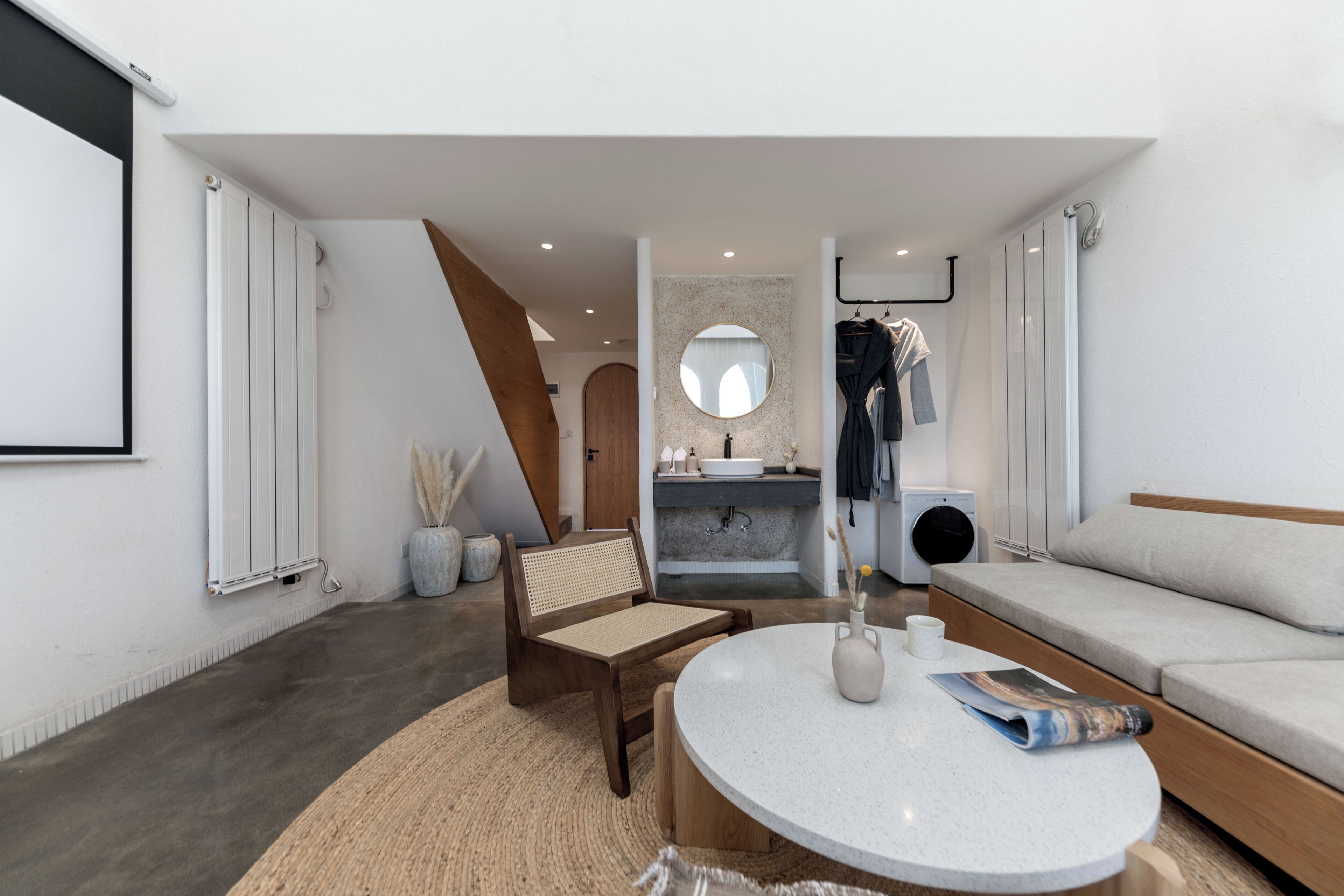A modern living room with a round table, a sofa, a chair, a round mirror, and a built-in washing machine.
