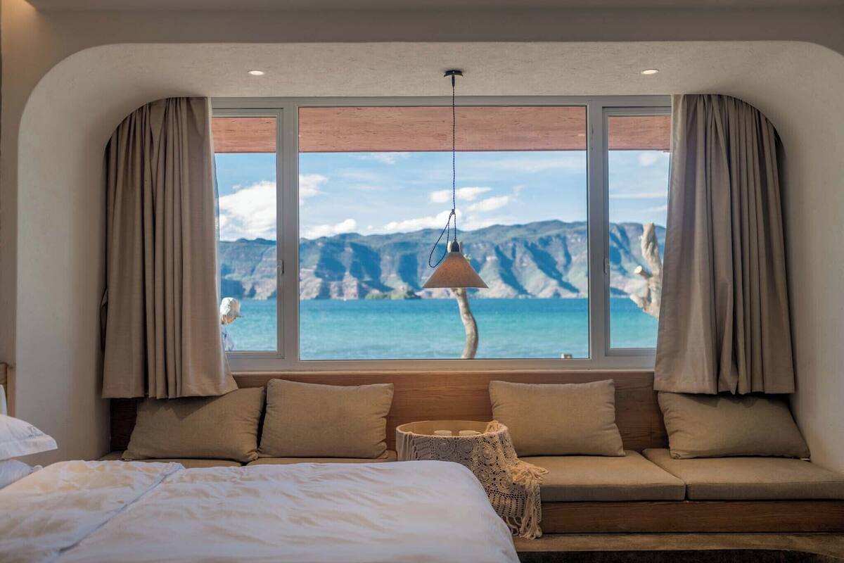 Ett sovrum med ett stort fönster, en säng, en soffa och en hängande lampa.