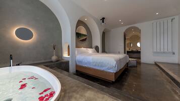 Une chambre moderne avec un grand lit, une baignoire remplie de pétales de roses et une salle de bain dotée d’un miroir et d’un radiateur.