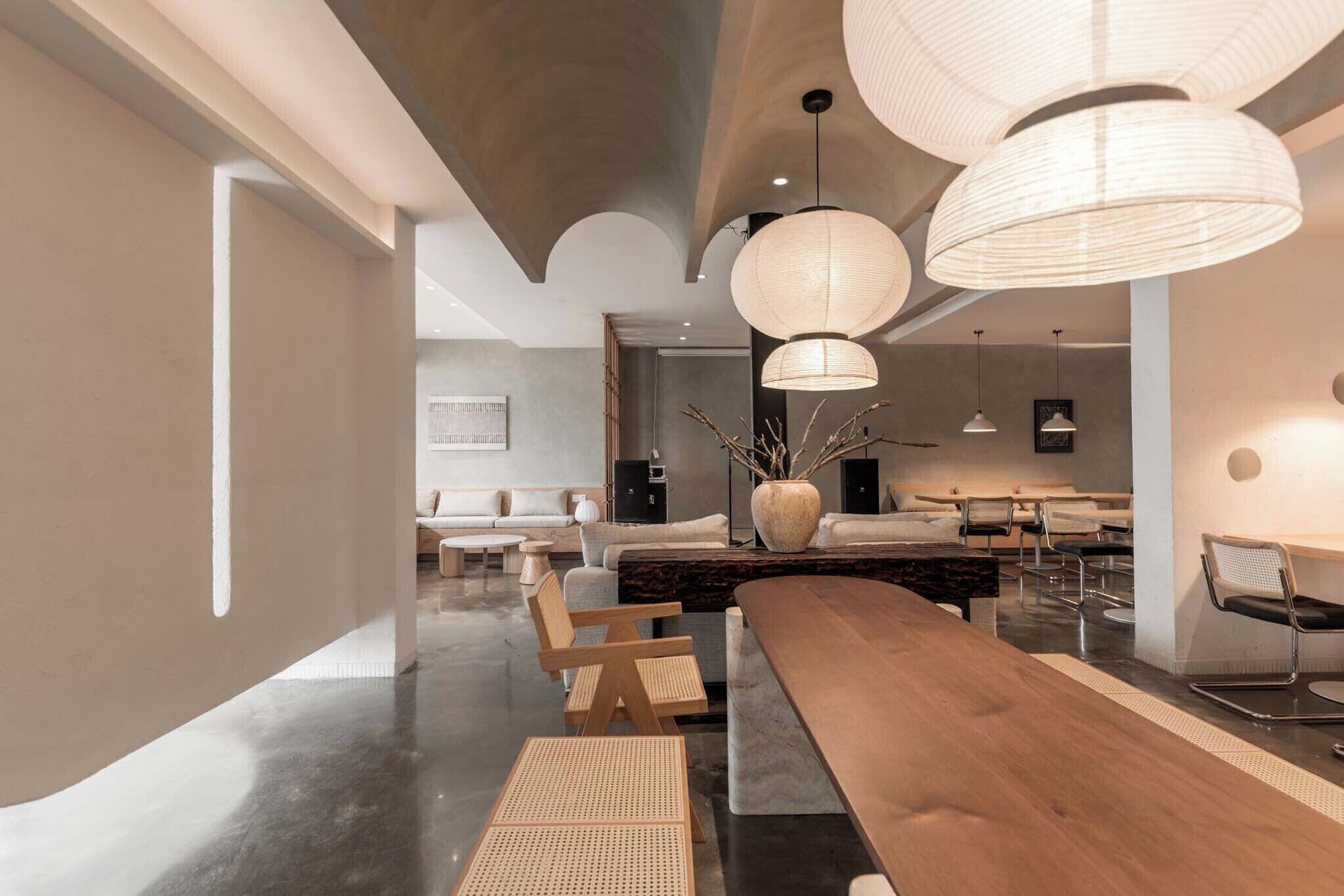 A modern interior with a long wooden table, multiple chairs, and a large vase with branches.