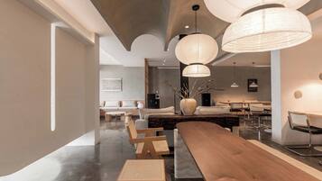 A modern interior with a long wooden table, multiple chairs, and a large vase with branches.
