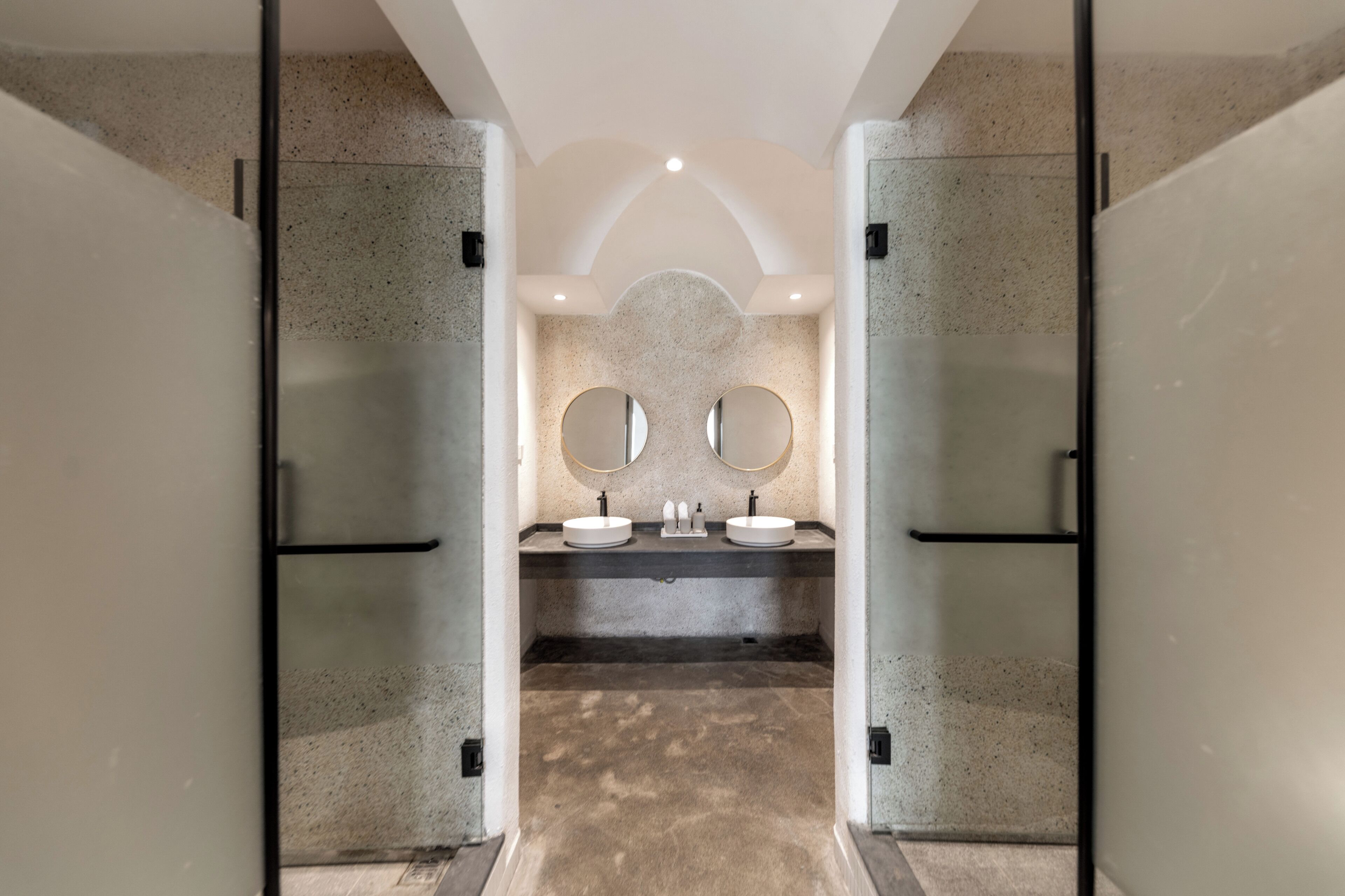 A modern bathroom with two sinks, a large mirror, and a speckled floor.