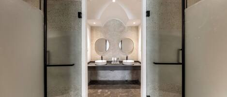 A modern bathroom with two sinks, a large mirror, and a speckled floor.
