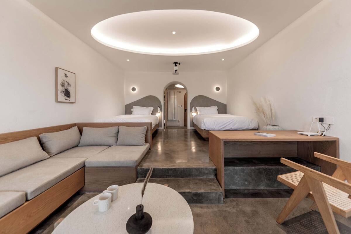 Ett modernt hotellrum med en soffa, två sängar, ett skrivbord och en rund taklampa.
