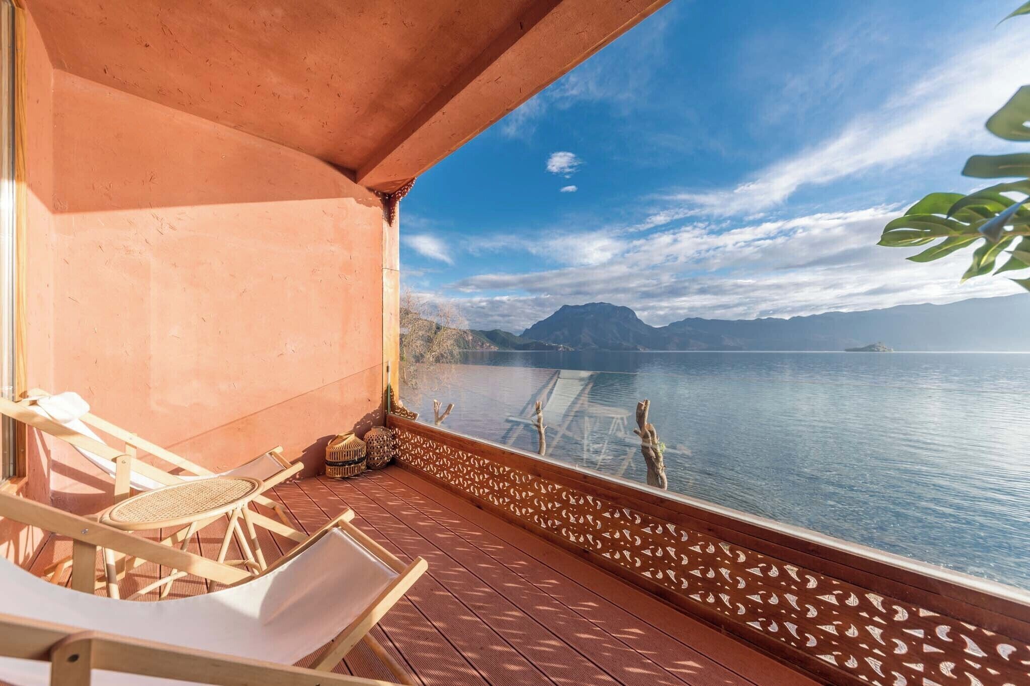 Un balcón con vistas a un lago tranquilo, mobiliario de madera y barandilla decorativa.